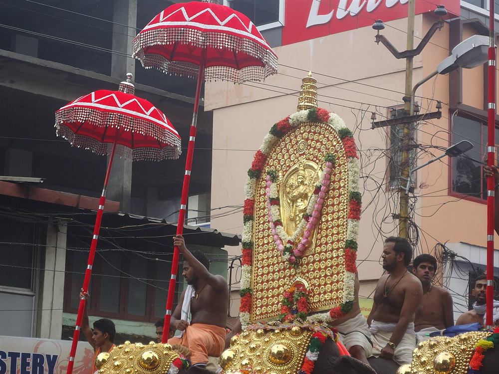 A caparisoned elephant under bright ceremonial umbrellas at a Kerala pooram